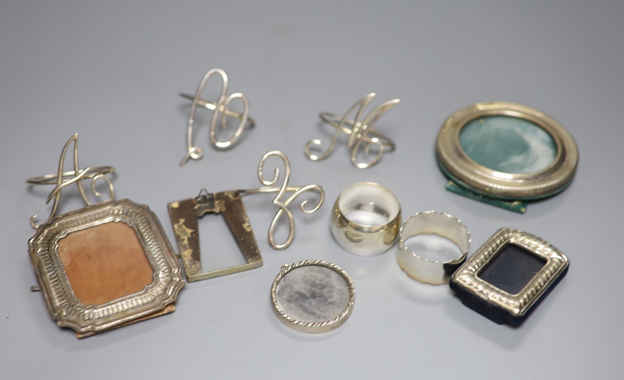 A set of four silver wire initial napkin rings, two other silver napkin rings (one Asprey) and five miniature photograph frames,